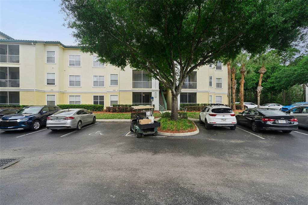 A multi-story apartment building exterior with a parking lot and a central tree — 8921 LEGACY COURT UNIT 18-308, KISSIMMEE, FL
