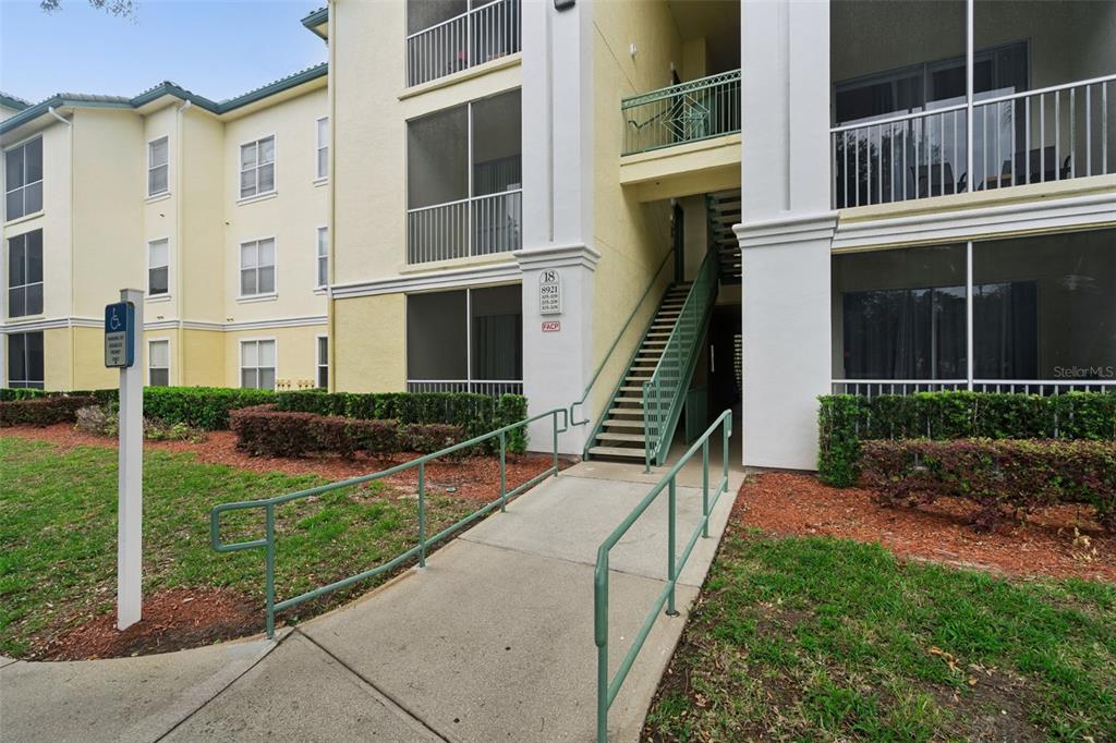 A concrete walkway with green railings leads to an exterior staircase of a yellow apartment building — 8921 LEGACY COURT UNIT 18-308, KISSIMMEE, FL