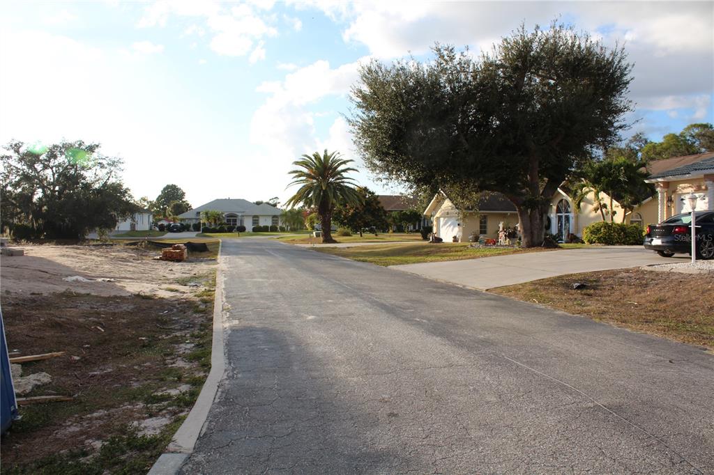 A paved residential street leads toward houses surrounded by trees and a palm tree — 2250 STONEGATE CIRCLE, PORT CHARLOTTE, FL