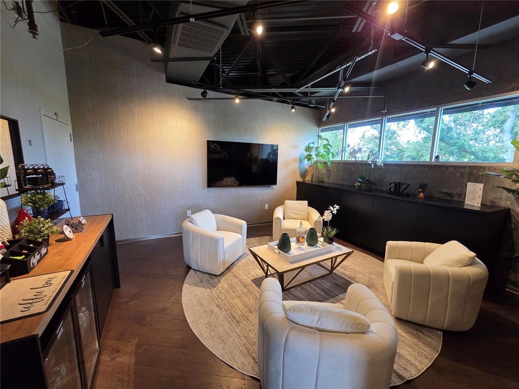 A lounge area features four white armchairs, a coffee table, and a wall-mounted television — 7802 KINGSPOINTE PARKWAY UNIT 202, ORLANDO, FL