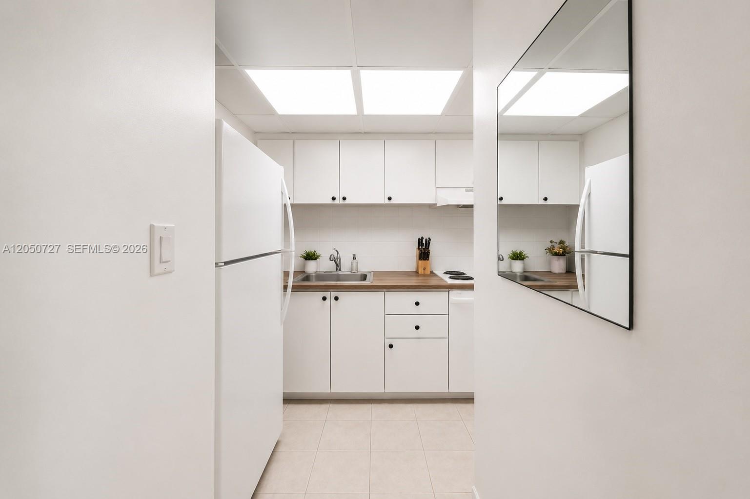 A white galley kitchen features wood countertops, white cabinetry, and a large wall mirror — 1200 West Ave, Miami Beach FL 33139, MIAMI BEACH, FL
