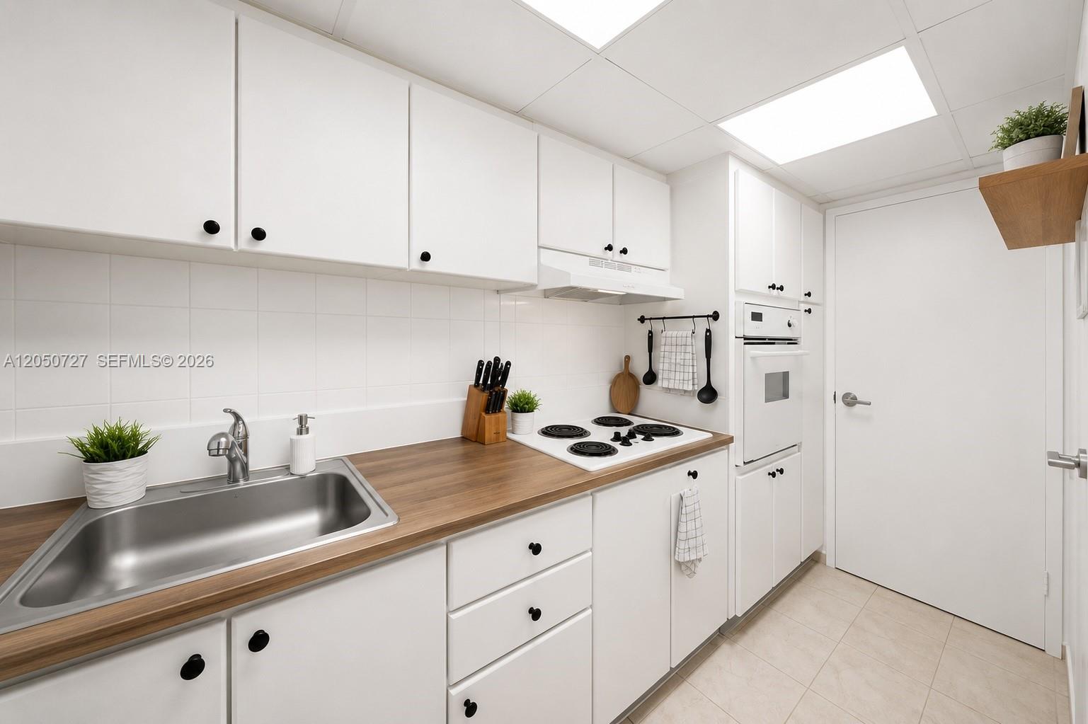 A galley kitchen features white cabinets, a wood countertop, and a built-in wall oven — 1200 West Ave, Miami Beach FL 33139, MIAMI BEACH, FL