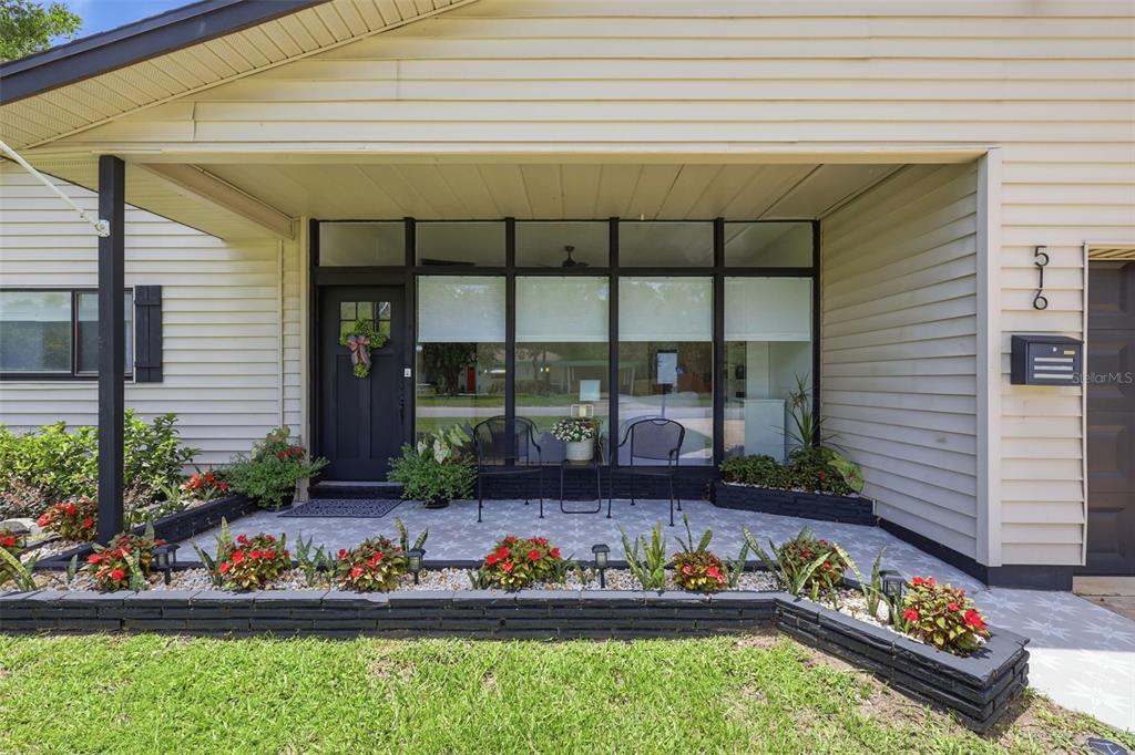 A front porch with a black door, large windows, and a landscaped brick planter bed — 516 N MCDONALD AVENUE, DELAND, FL