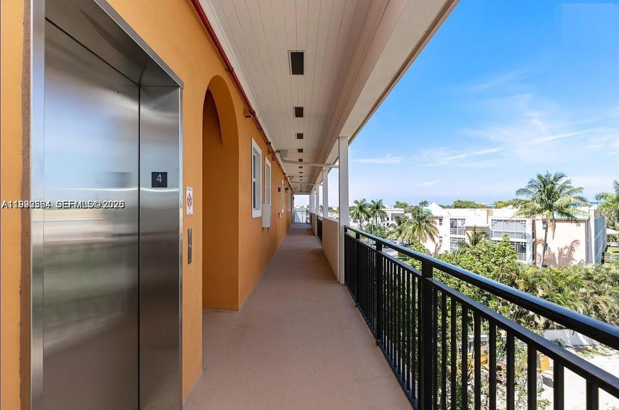 An outdoor apartment hallway features an elevator, orange walls, and a black metal railing — 555 E Dania Beach Blvd # 5, Dania Beach FL 33004, DANIA BEACH, FL