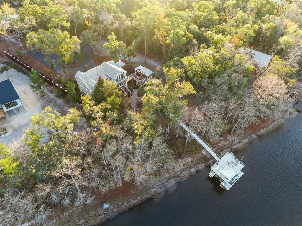 An aerial view shows a multi-story house with a private dock extending into the water — 174 NE 972ND STREET, BRANFORD, FL