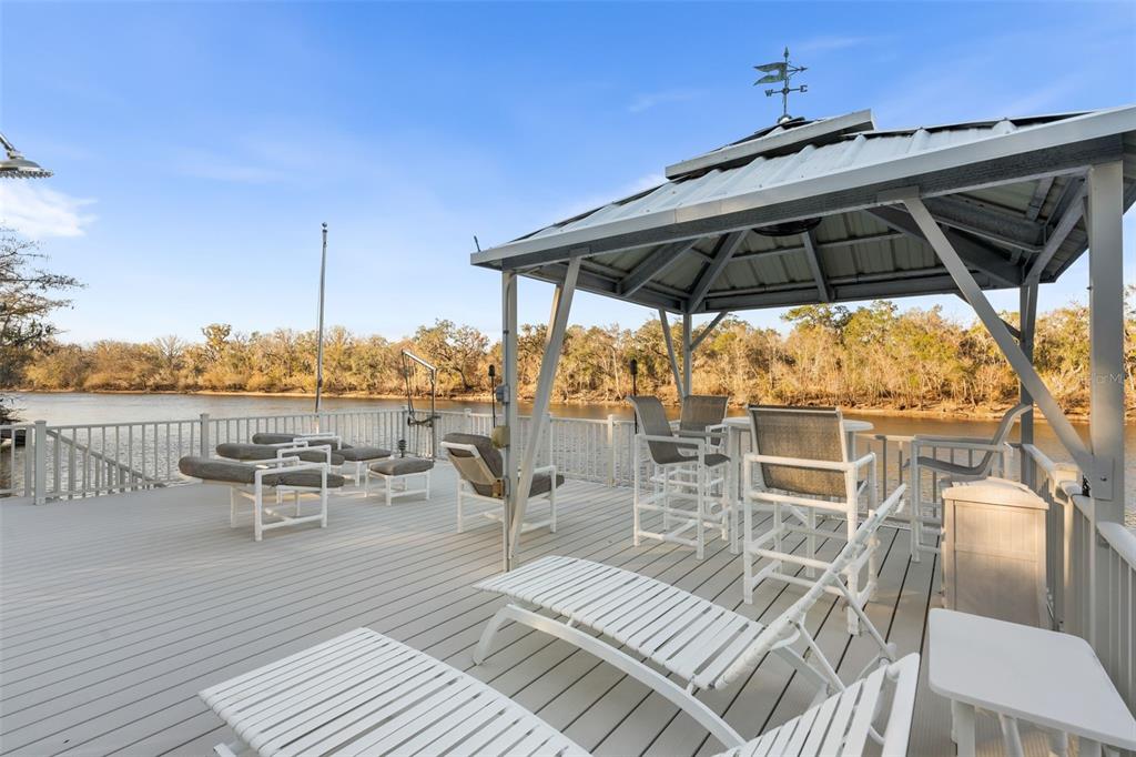 A wooden deck overlooking a river features a metal gazebo and several outdoor lounge chairs — 174 NE 972ND STREET, BRANFORD, FL