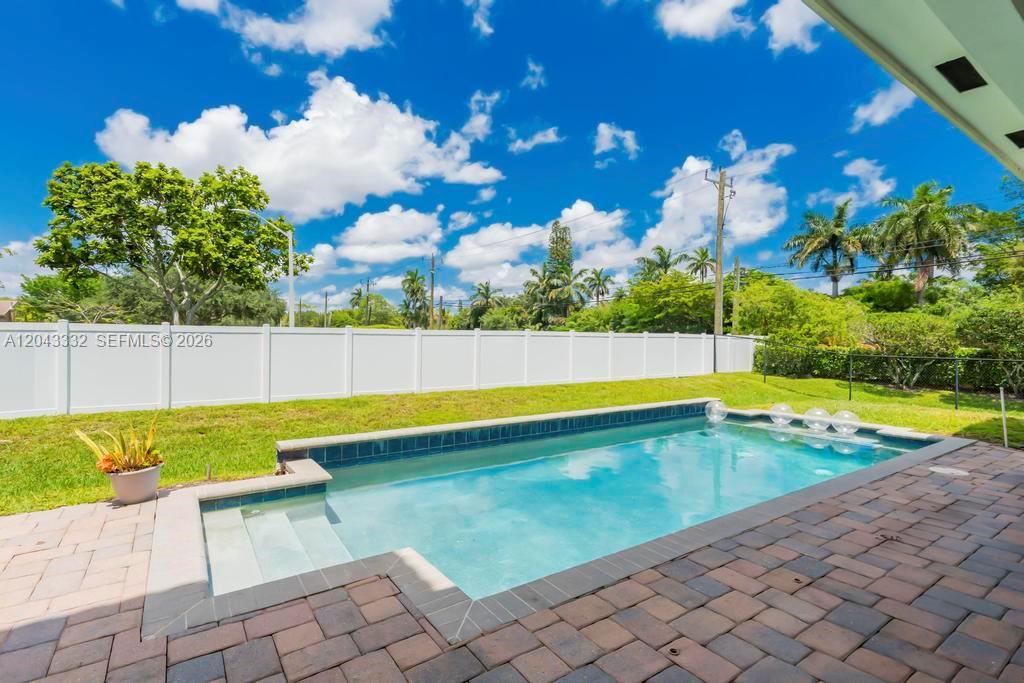 A rectangular swimming pool sits in a backyard with a white fence and patio — 7601 Cavalia Dr, Davie FL 33328, DAVIE, FL
