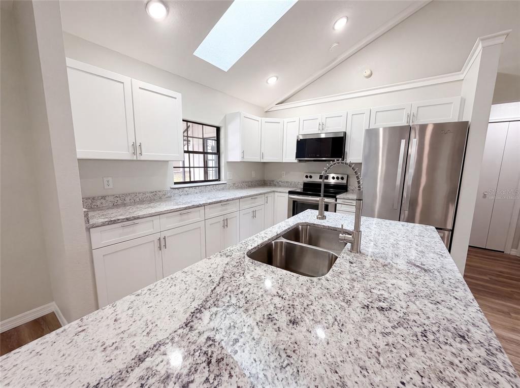 A kitchen features white cabinets, granite countertops, a central island with a sink, and stainless appliances — 5082 SW 31ST STREET, OCALA, FL