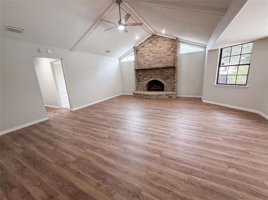 A living room features a vaulted ceiling, wood-look flooring, and a large brick fireplace — 5082 SW 31ST STREET, OCALA, FL