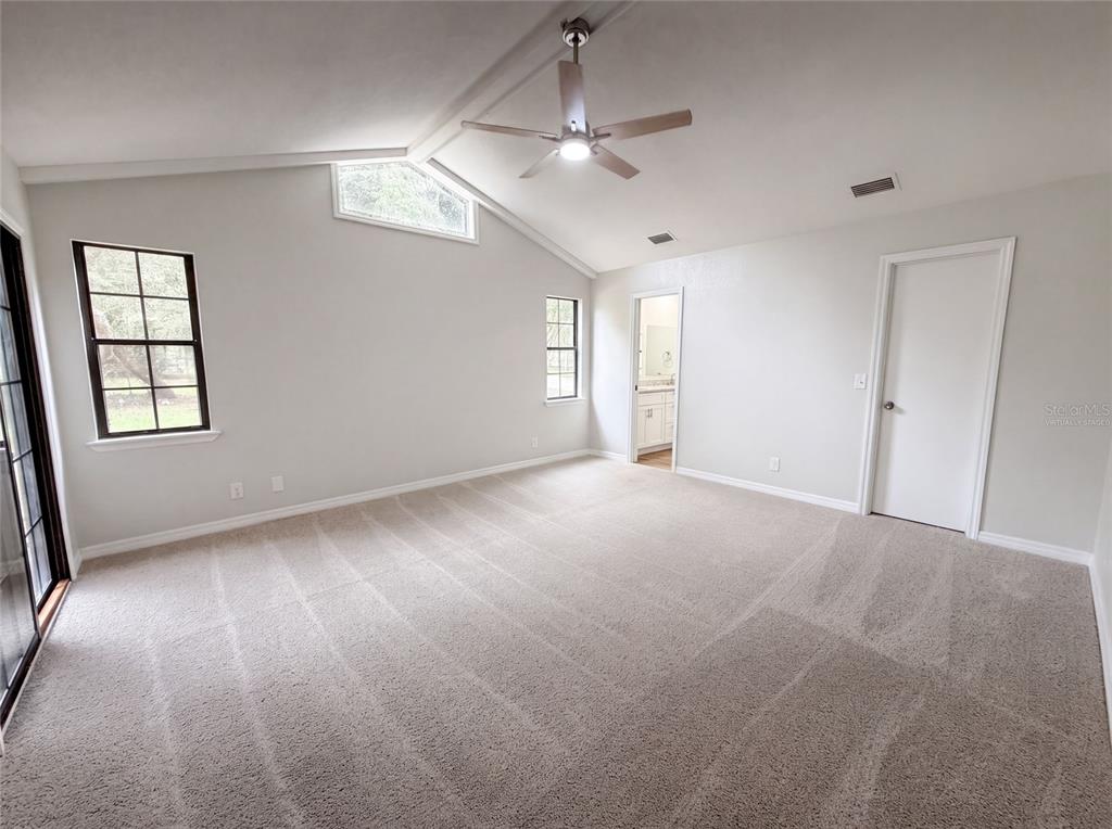A bedroom with vaulted ceilings, a ceiling fan, carpeted floors, and an attached bathroom — 5082 SW 31ST STREET, OCALA, FL