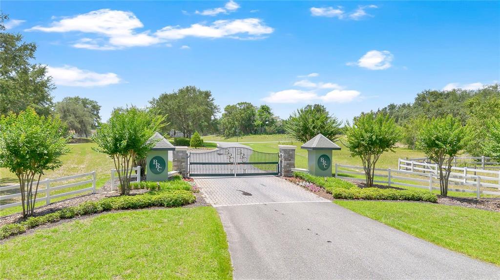 A paved driveway leads to a gated entrance with stone pillars and white fencing — GRAND OAK LANE, TAVARES, FL