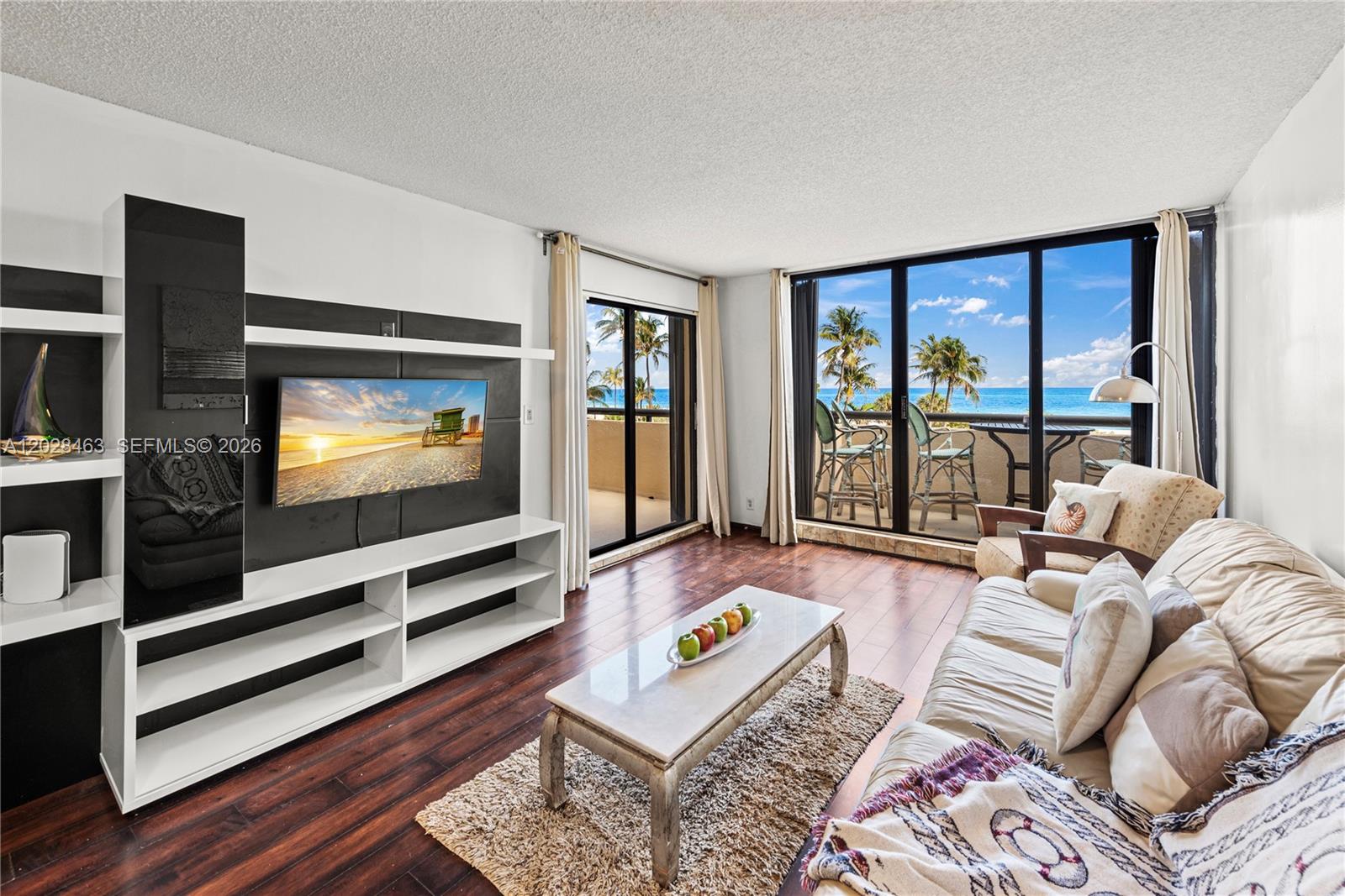A living room features a wall-mounted television, white shelving, a sofa, and ocean views — 2555 Collins Ave # 403, Miami Beach FL 33140, MIAMI BEACH, FL
