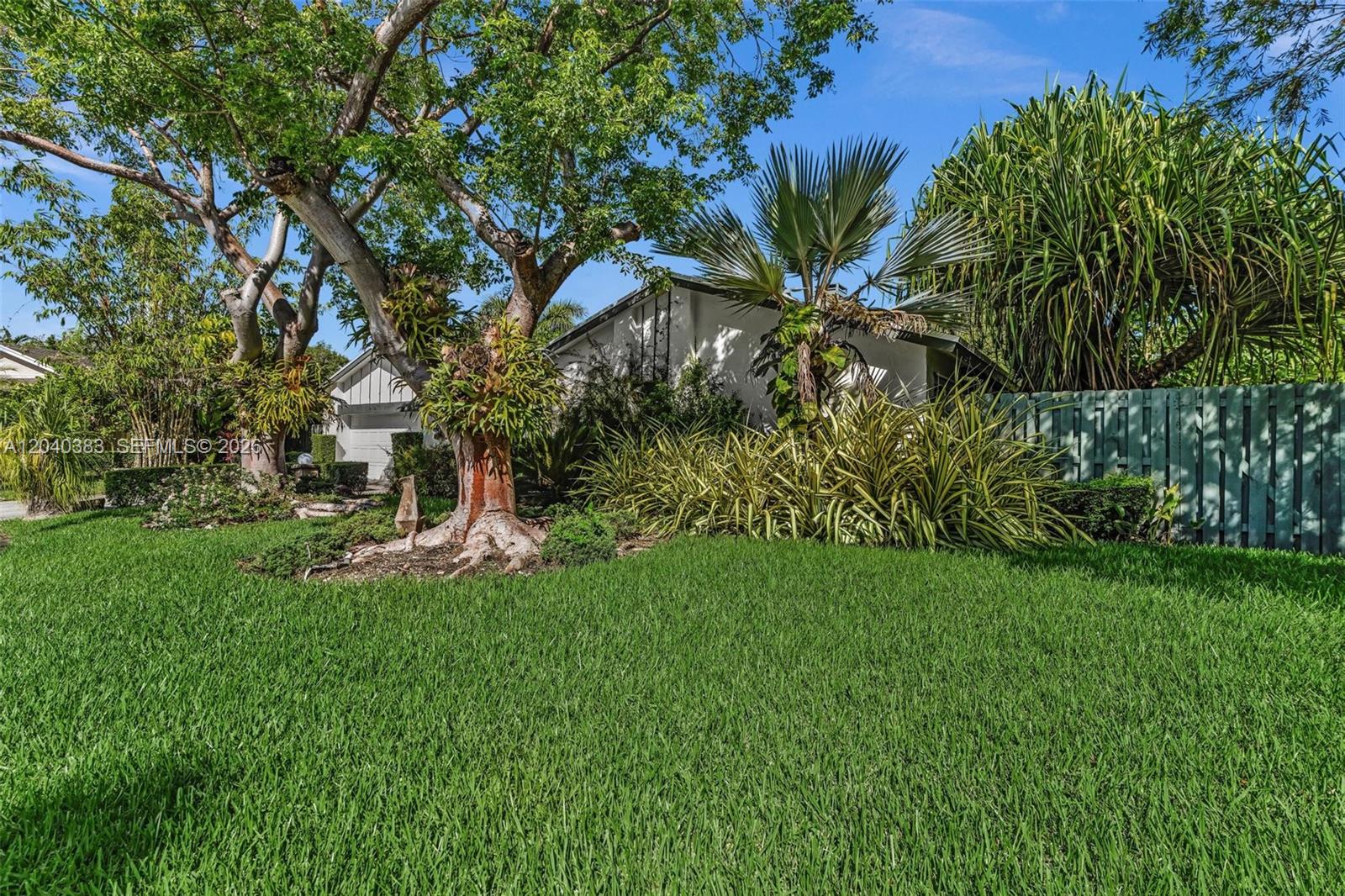 A single-story house is partially obscured by large trees and lush tropical landscaping — 10612 SW 128th Pl, Miami FL 33186, MIAMI, FL