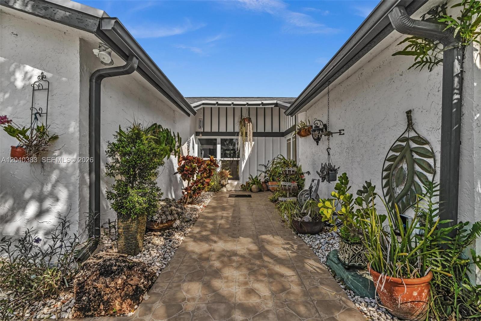 A tiled walkway leads to a home entrance flanked by white stucco walls and plants — 10612 SW 128th Pl, Miami FL 33186, MIAMI, FL