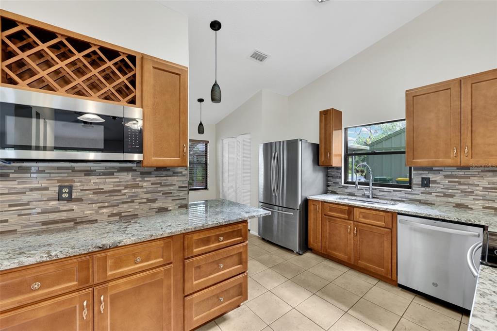 A kitchen features wood cabinets, granite countertops, stainless steel appliances, and a tiled backsplash — 5015 BARRINGTON CIRCLE UNIT 201, SARASOTA, FL