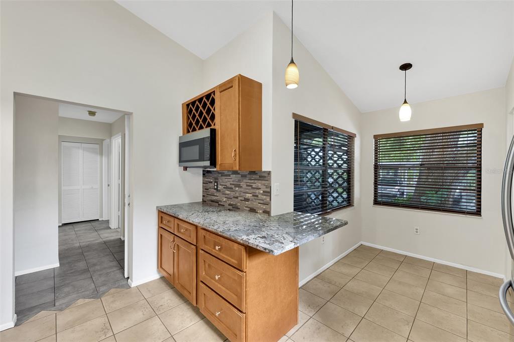A kitchen with wood cabinets, granite countertops, a tiled backsplash, and a dining area — 5015 BARRINGTON CIRCLE UNIT 201, SARASOTA, FL