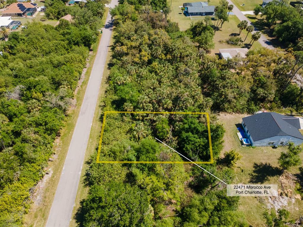 An aerial view shows a rectangular vacant lot surrounded by dense vegetation and nearby houses — 22471 MOROCCO AVENUE, PORT CHARLOTTE, FL