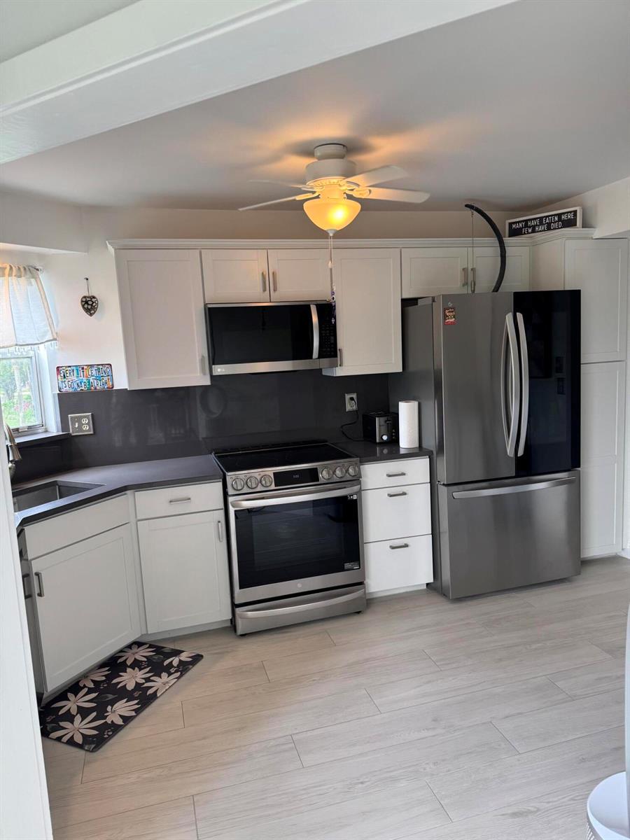 A kitchen features white cabinets, stainless steel appliances, a dark backsplash, and light wood flooring — 3590 Via # 312, Lake Worth FL 33467, LAKE WORTH, FL