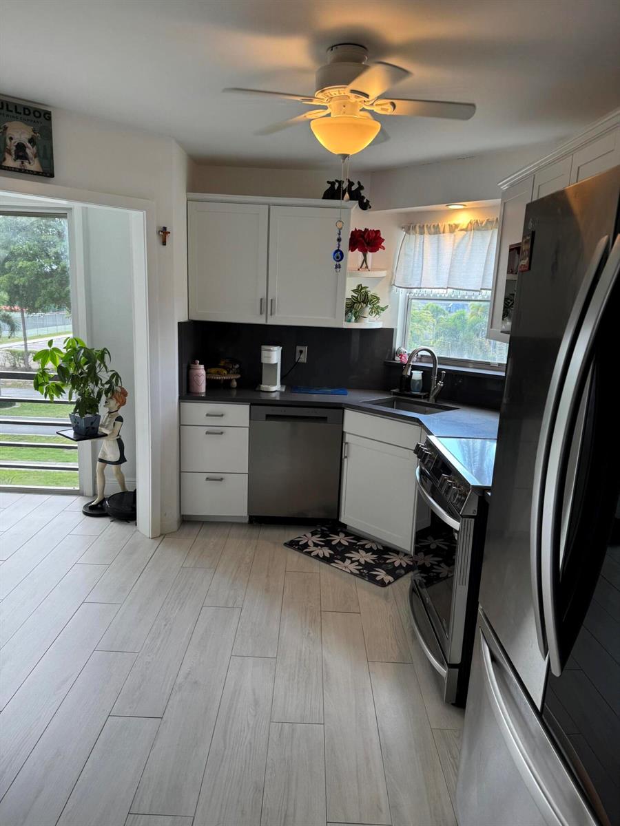 A kitchen features white cabinets, stainless steel appliances, dark countertops, and light wood-look tile flooring — 3590 Via # 312, Lake Worth FL 33467, LAKE WORTH, FL