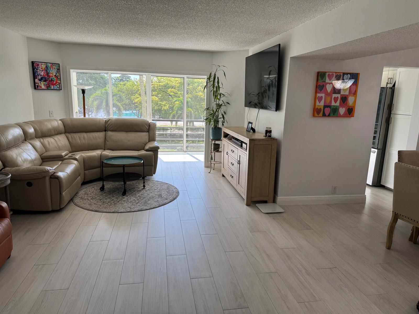 A living room features a beige sectional sofa, light wood flooring, and a wall-mounted television — 3590 Via # 312, Lake Worth FL 33467, LAKE WORTH, FL
