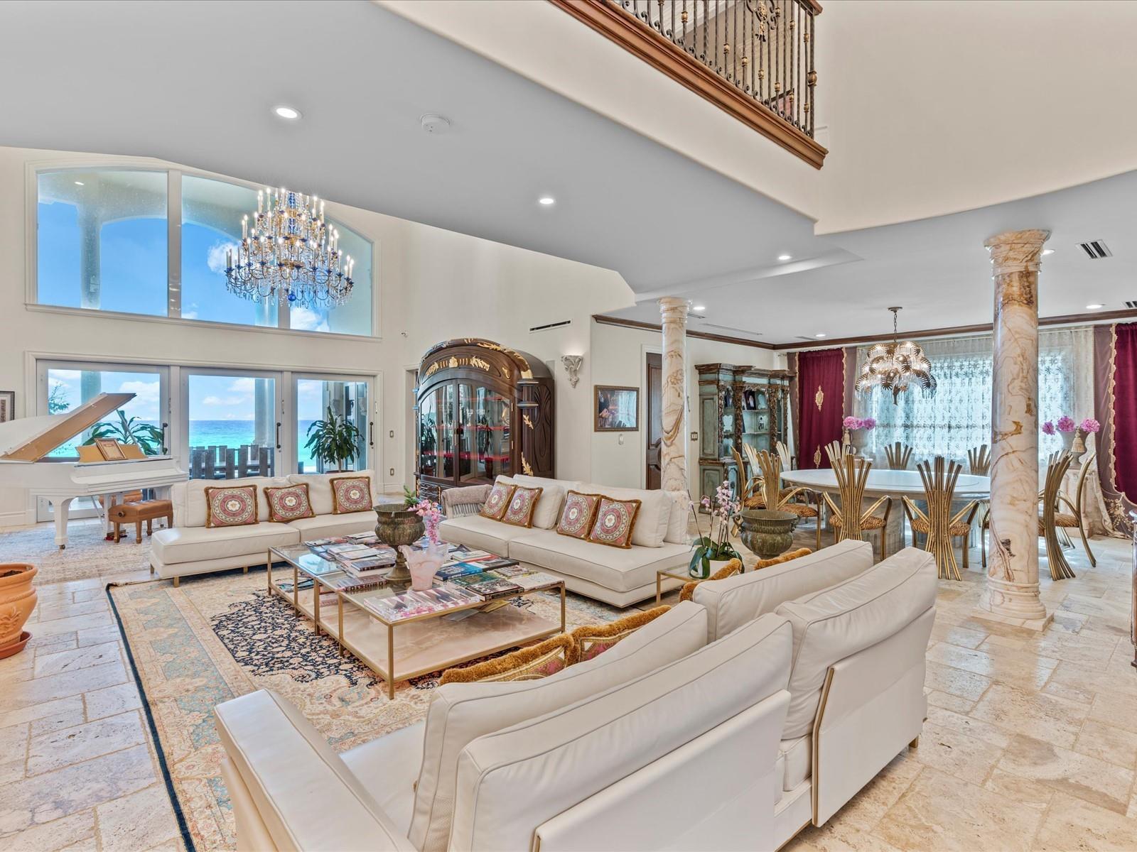 A spacious living and dining area with white sofas, a grand piano, and ocean views — 555 Ocean Boulevard, Golden Beach FL 33160, GOLDEN BEACH, FL