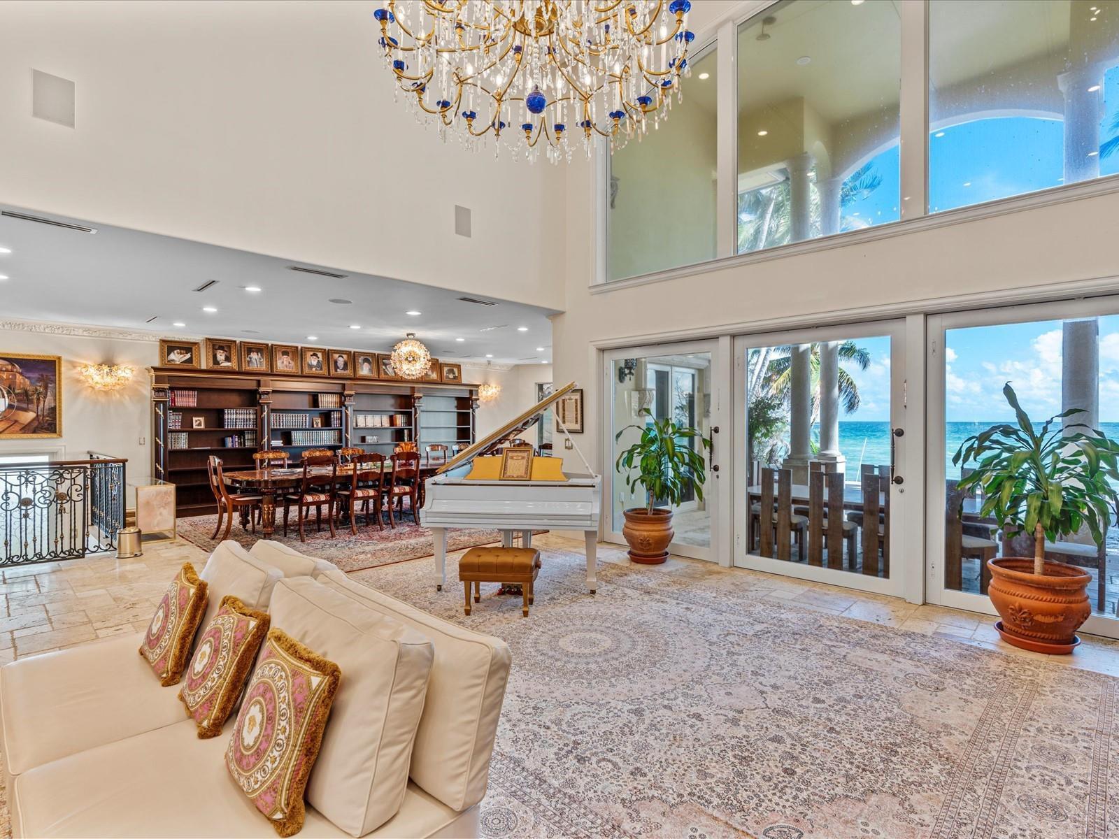 A spacious living room features a white grand piano, a dining area, and ocean views — 555 Ocean Boulevard, Golden Beach FL 33160, GOLDEN BEACH, FL