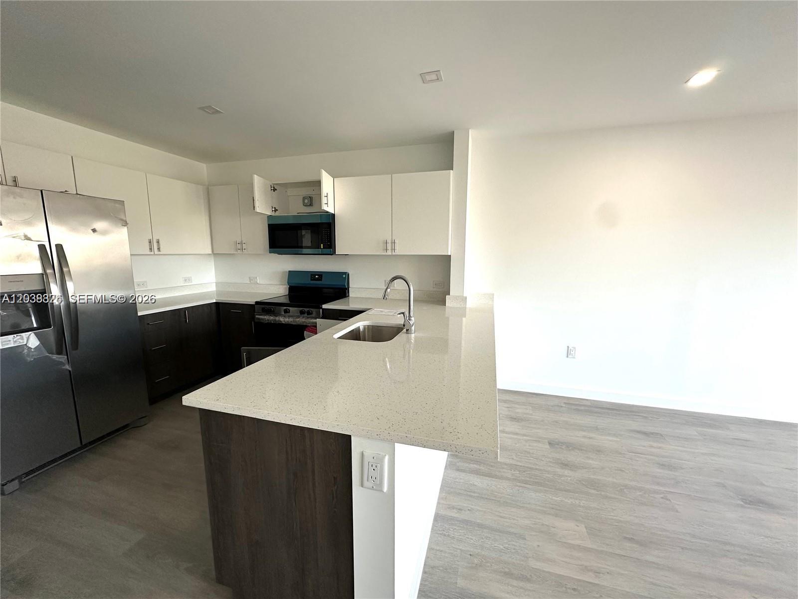 A kitchen features white upper cabinets, dark lower cabinets, a stainless refrigerator, and a peninsula — 20 NE 19th Ave # 213, Pompano Beach FL 33060, POMPANO BEACH, FL