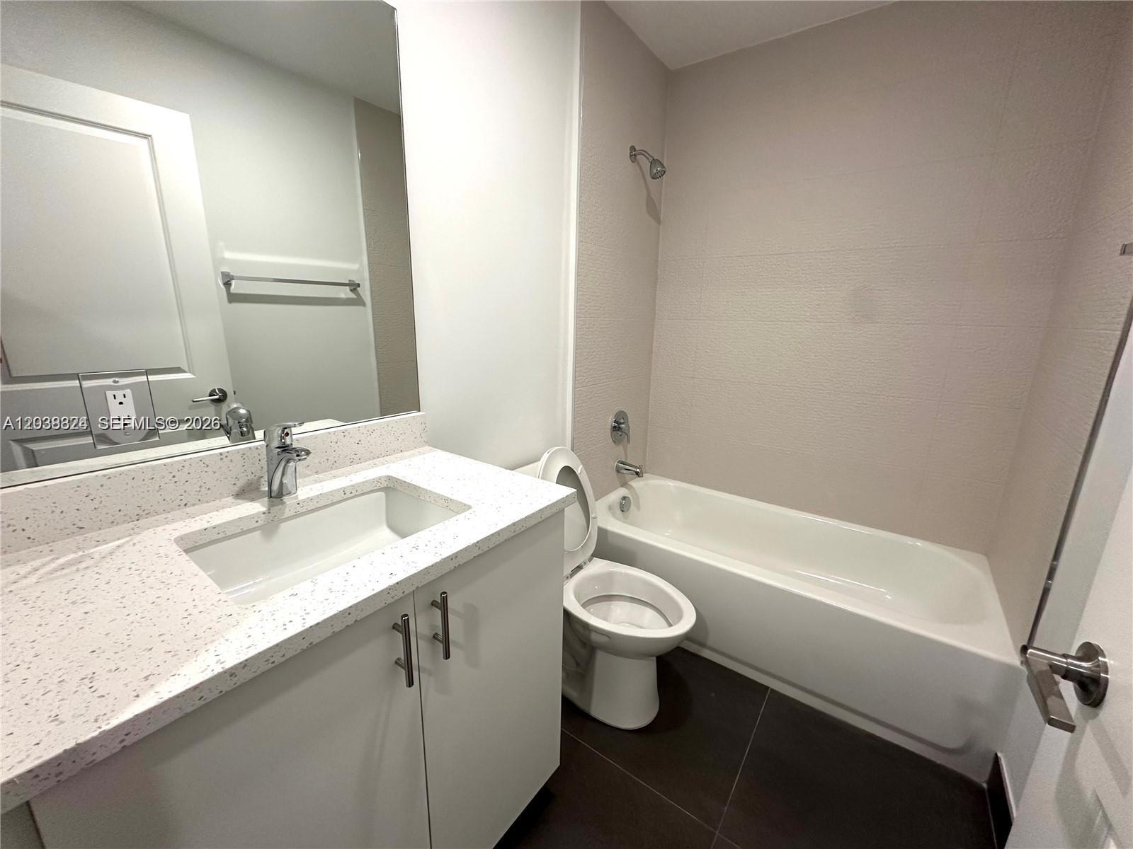 A bathroom features a white vanity with a speckled countertop, toilet, and a shower-tub combo — 20 NE 19th Ave # 213, Pompano Beach FL 33060, POMPANO BEACH, FL