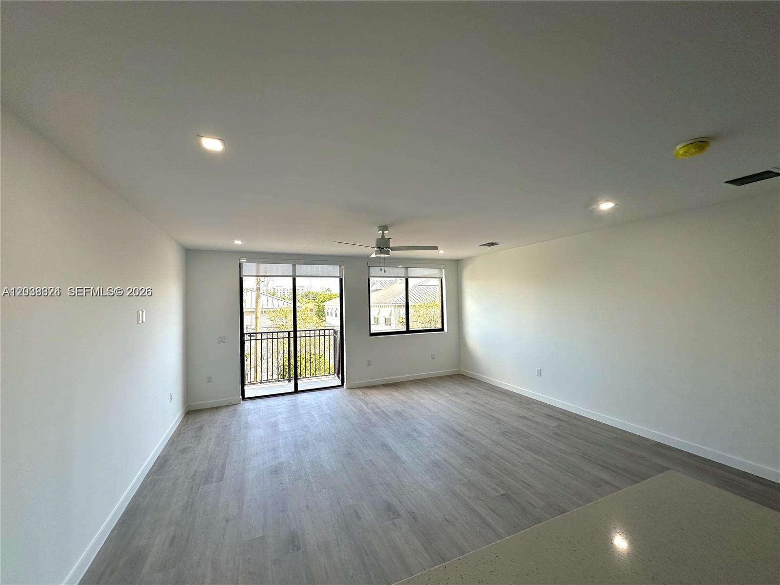 An empty living room features light wood-look flooring, white walls, a ceiling fan, and a balcony — 20 NE 19th Ave # 213, Pompano Beach FL 33060, POMPANO BEACH, FL