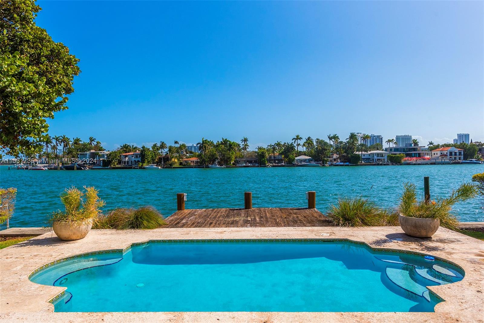 A swimming pool sits on a stone patio overlooking a wooden dock and the water — 527 E Dilido Dr, Miami Beach FL 33139, MIAMI BEACH, FL