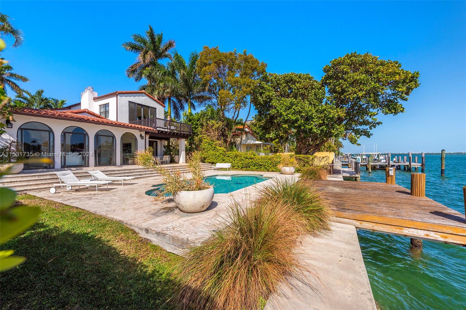 A waterfront home features a swimming pool, stone patio, and a wooden dock — 527 E Dilido Dr, Miami Beach FL 33139, MIAMI BEACH, FL
