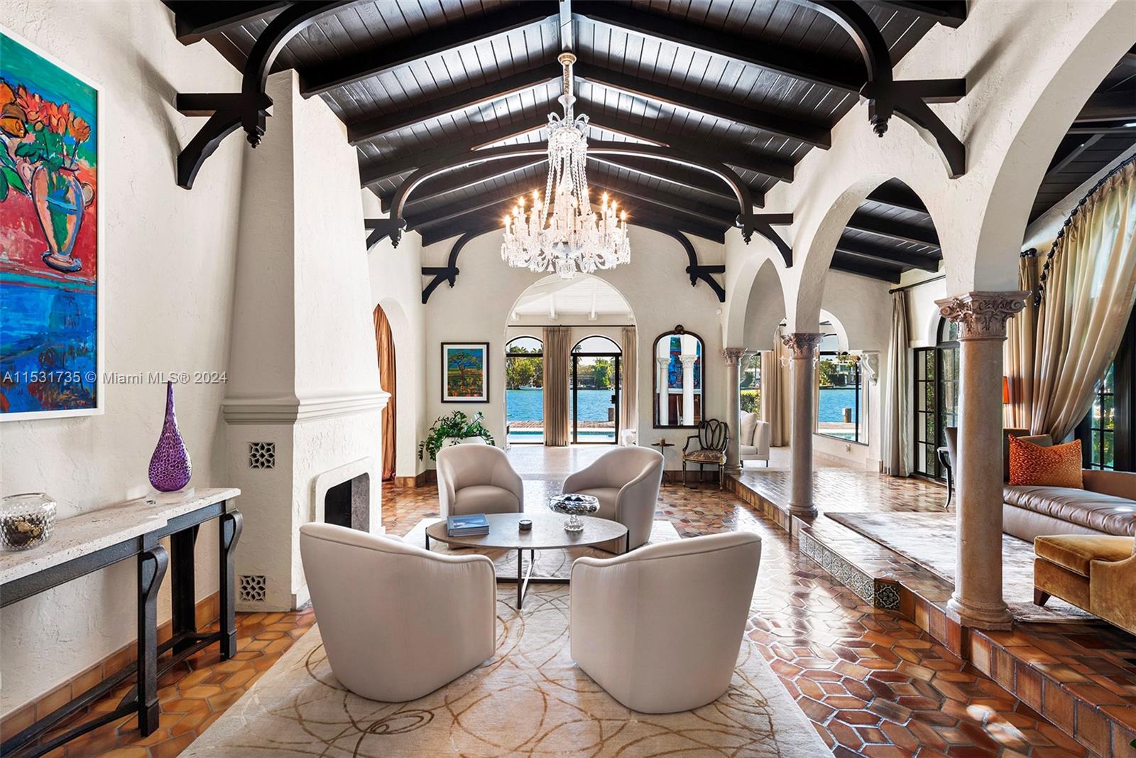 A spacious living room features a vaulted wood-beamed ceiling, crystal chandelier, and terracotta tile floors — 527 E Dilido Dr, Miami Beach FL 33139, MIAMI BEACH, FL