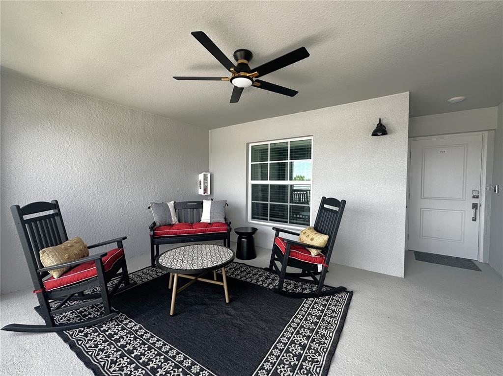 A covered patio features a ceiling fan, black rocking chairs, a bench, and a patterned rug — 14251 HERITAGE LANDING BOULEVARD UNIT 1723, PUNTA GORDA, FL