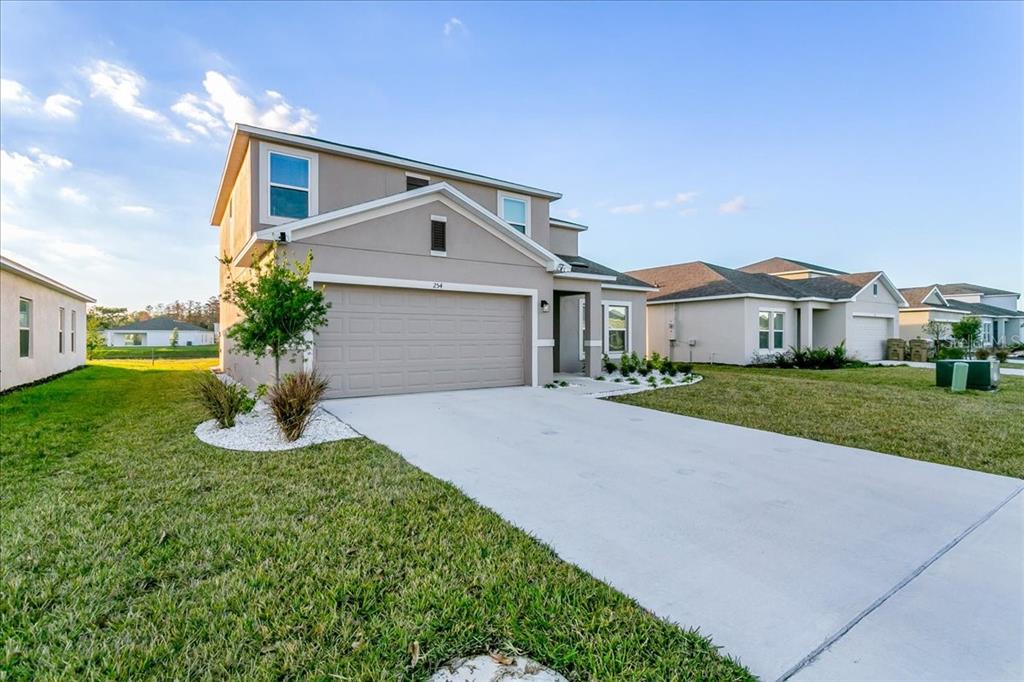 A two-story suburban house features a beige stucco exterior, a two-car garage, and a concrete driveway — 254 AMBER WAY, KISSIMMEE, FL