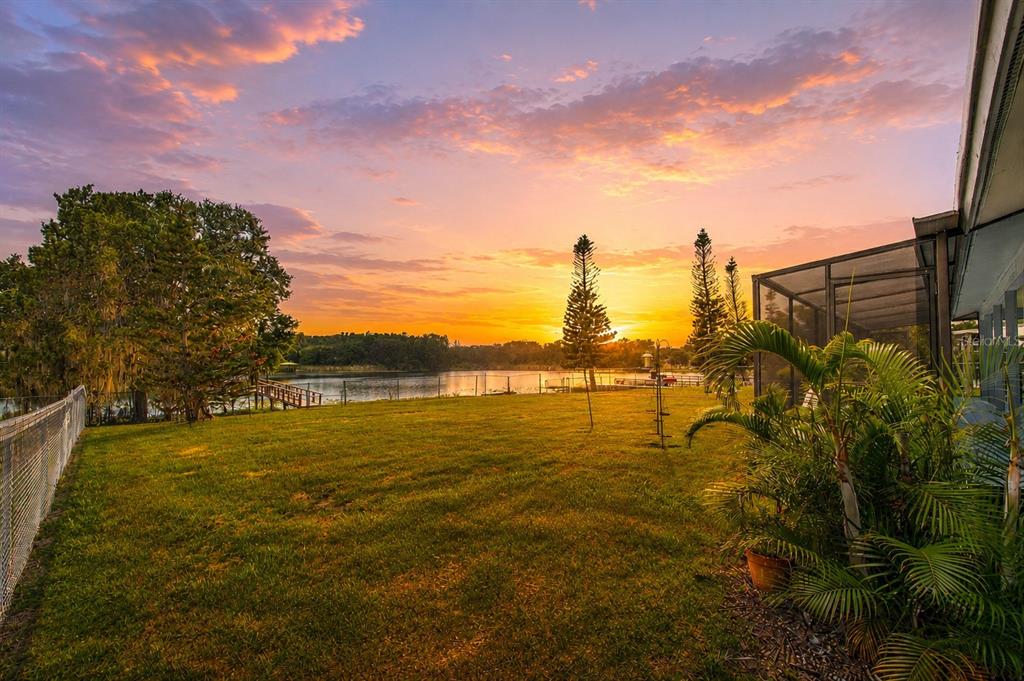 A grassy backyard overlooks a lake at sunset with a screened-in patio on the right — 2459 SHOREWOOD LANE, LAND O LAKES, FL