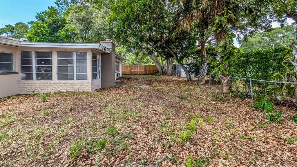 The exterior of a beige, single-story house features a large, leaf-covered backyard and mature trees — 611 PATRICIA AVENUE, DUNEDIN, FL