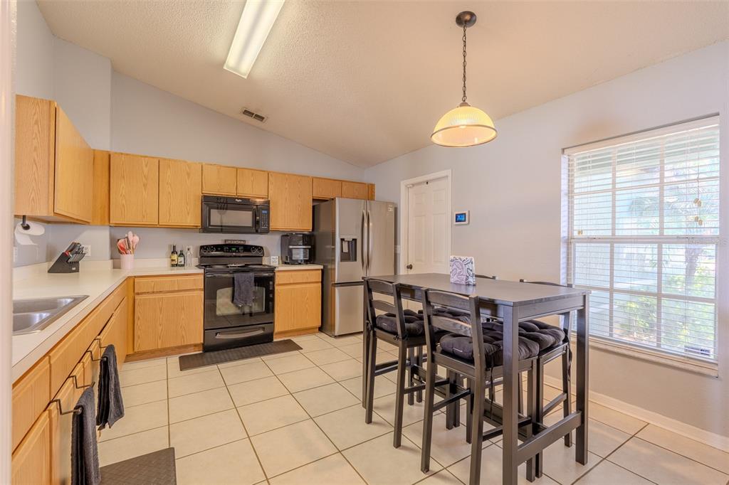 A kitchen with light wood cabinets, black appliances, tile flooring, and a dining table — 145 EAGLE POINT BOULEVARD, AUBURNDALE, FL