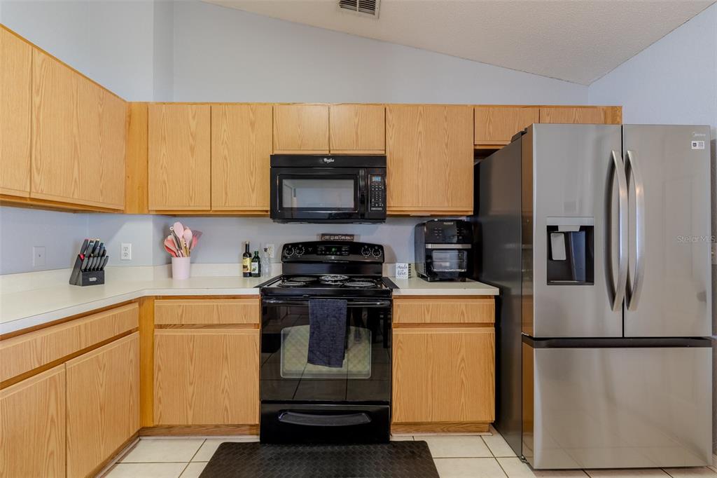 A kitchen features light wood cabinets, black appliances, a stainless steel refrigerator, and white countertops — 145 EAGLE POINT BOULEVARD, AUBURNDALE, FL