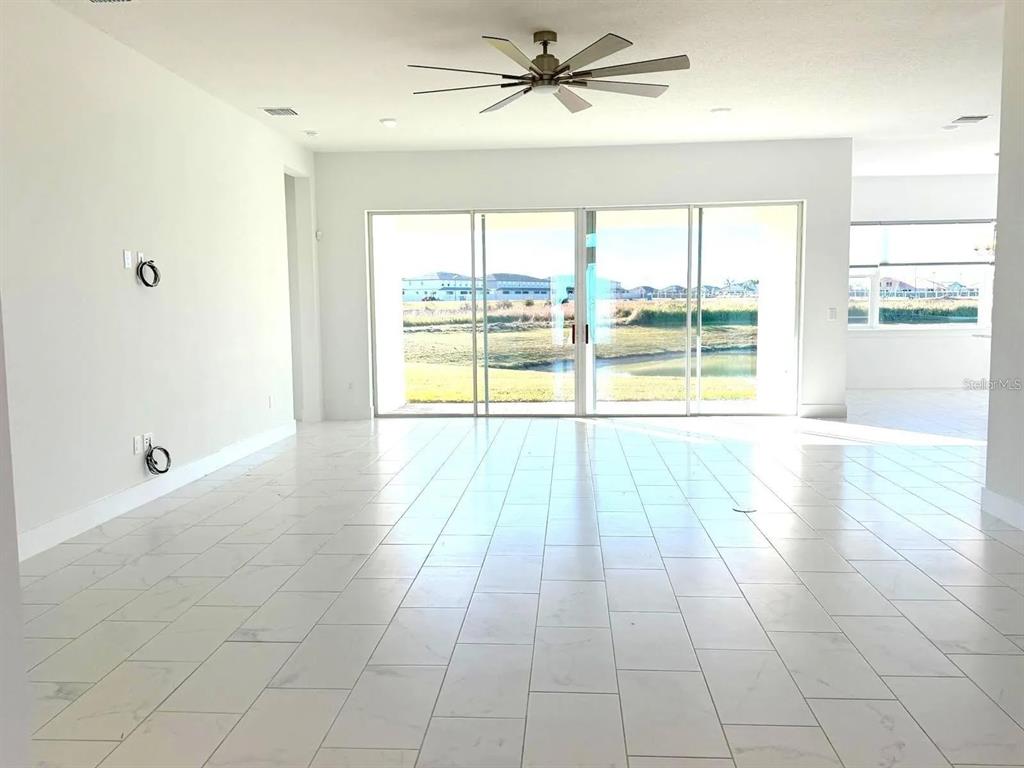 A bright living room features white tile flooring, a ceiling fan, and large sliding glass doors — 10609 TORCHWOOD SEA WAY, SAN ANTONIO, FL