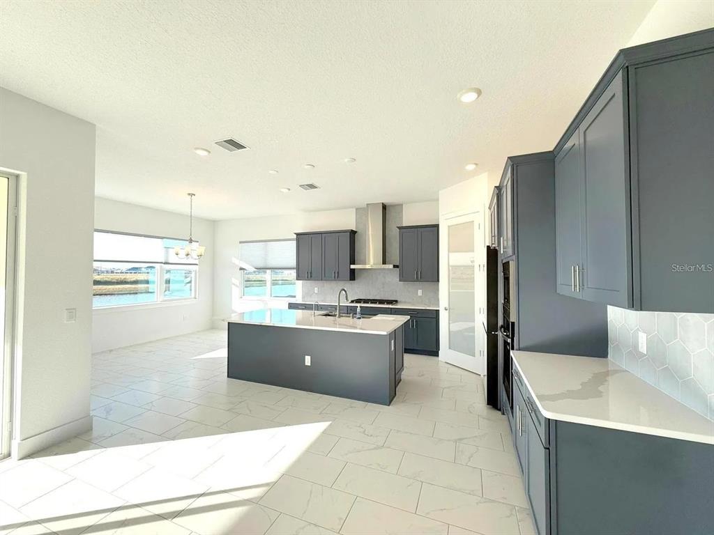 A modern kitchen features dark blue cabinetry, a central island, and white tile flooring — 10609 TORCHWOOD SEA WAY, SAN ANTONIO, FL