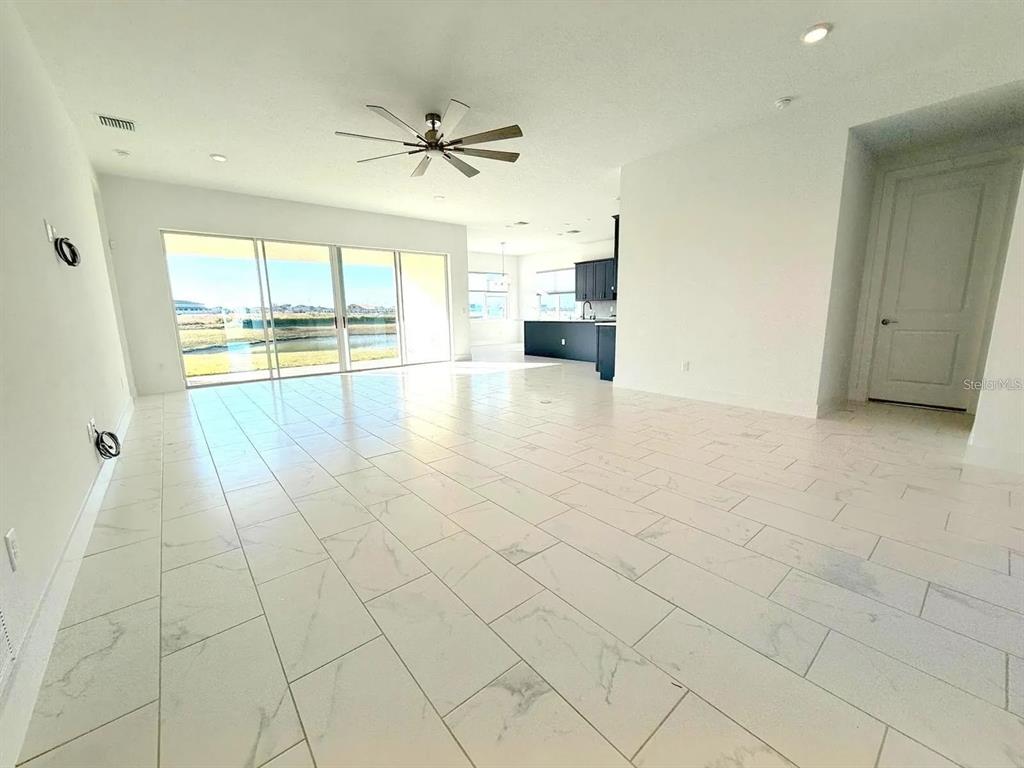 An open-concept living area features white marble-look tile flooring, a ceiling fan, and sliding doors — 10609 TORCHWOOD SEA WAY, SAN ANTONIO, FL