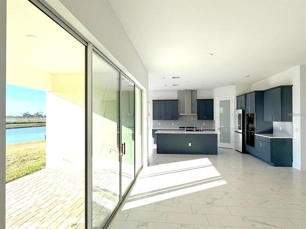 A modern kitchen with dark blue cabinetry and a center island overlooks a waterfront patio — 10609 TORCHWOOD SEA WAY, SAN ANTONIO, FL