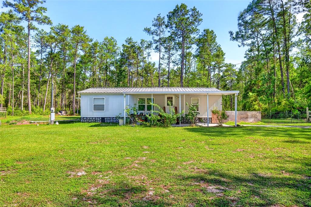A single-story manufactured home with a metal roof sits on a grassy lot near trees — 16240 NE 141ST TERRACE, FORT MC COY, FL