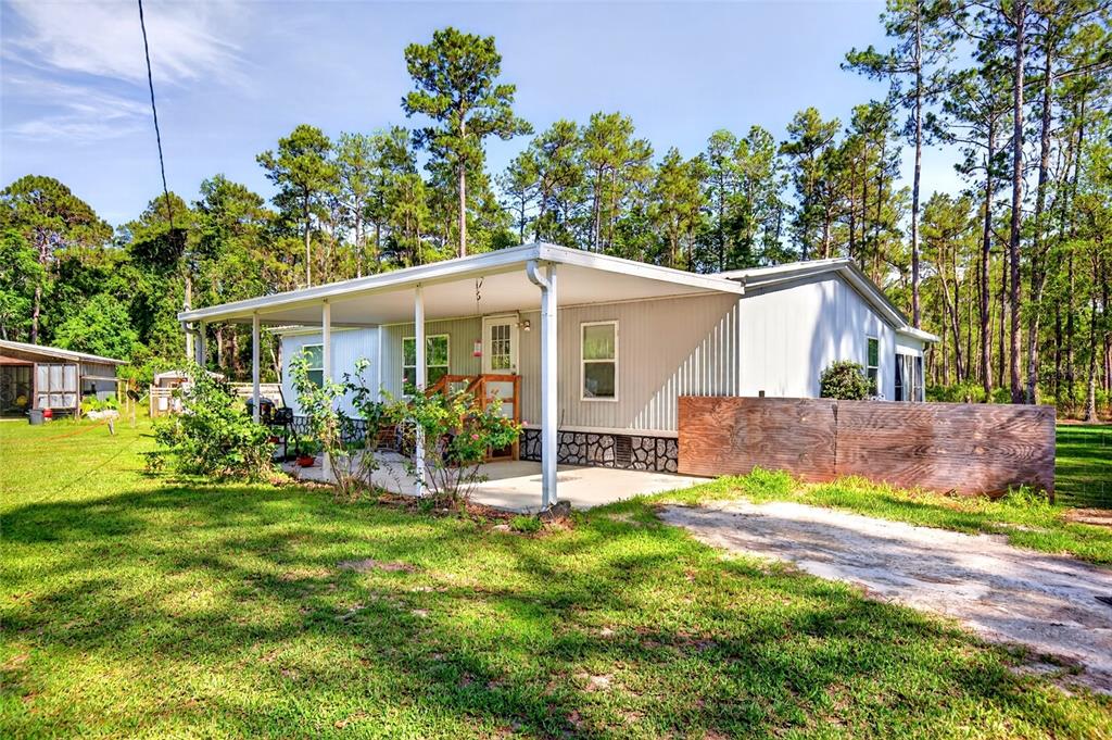 A single-story manufactured home features a covered front porch and a wooden privacy fence — 16240 NE 141ST TERRACE, FORT MC COY, FL