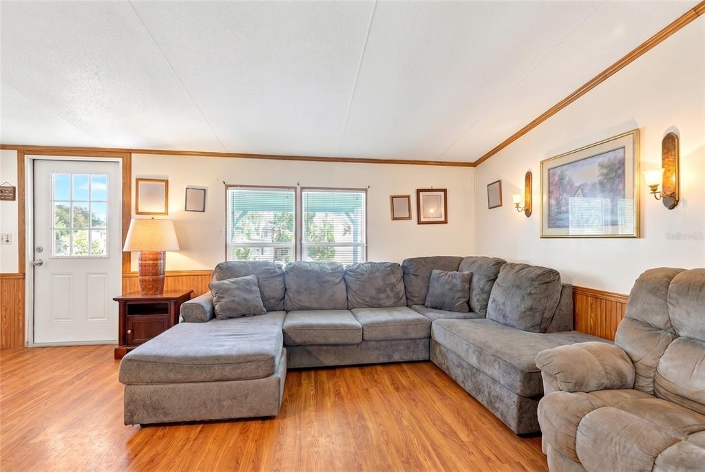 A living room features a gray sectional sofa, wood-look flooring, and wood wainscoting — 16240 NE 141ST TERRACE, FORT MC COY, FL