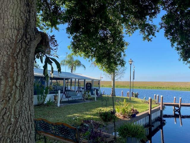 A waterfront backyard features a screened patio, a wooden bench, and a dock by the water — 8680 Us Highway 441 SE # 35, Okeechobee FL 34974, OKEECHOBEE, FL