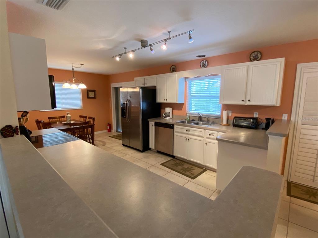 A kitchen features white cabinets, stainless steel appliances, and a breakfast bar with gray countertops — 1808 N PENINSULA AVENUE, NEW SMYRNA BEACH, FL