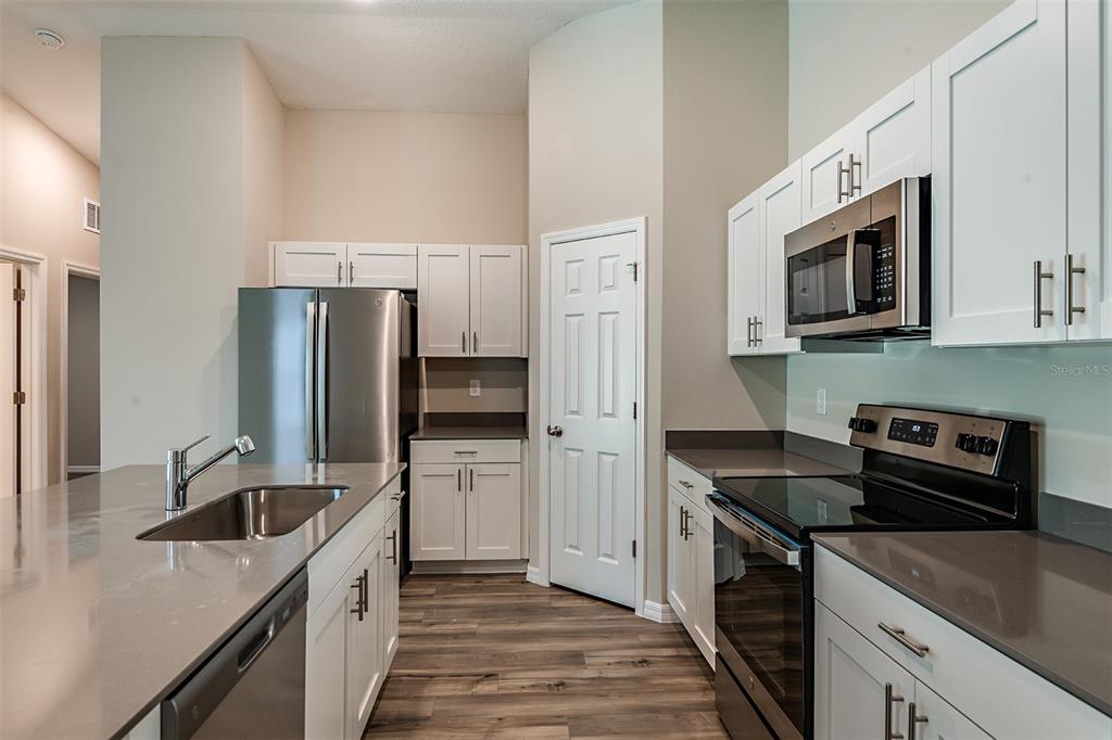 A kitchen features white cabinets, stainless steel appliances, a center island, and wood-look flooring — 4449 RIVERBEND BOULEVARD, HAINES CITY, FL