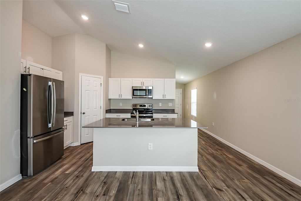 A kitchen features white cabinets, stainless steel appliances, a center island, and wood-look flooring — 4449 RIVERBEND BOULEVARD, HAINES CITY, FL