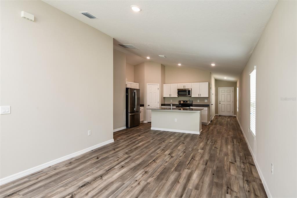 An open-concept kitchen features white cabinetry, a center island, and wood-look flooring — 4449 RIVERBEND BOULEVARD, HAINES CITY, FL